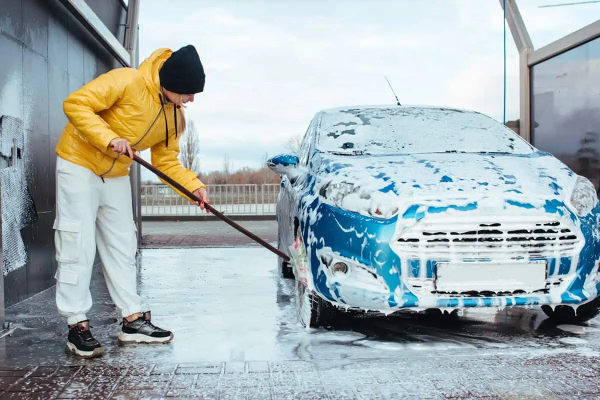 A man in a big yellow coat, washing a car in winter