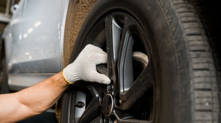Gloved mechanic hand inspecting a car tire on a black wheel