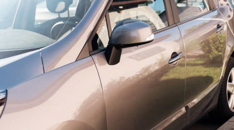 The side of a shiny, silver car including front door to rear wheel