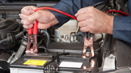 Man plugging cables from a car battery charger onto the battery