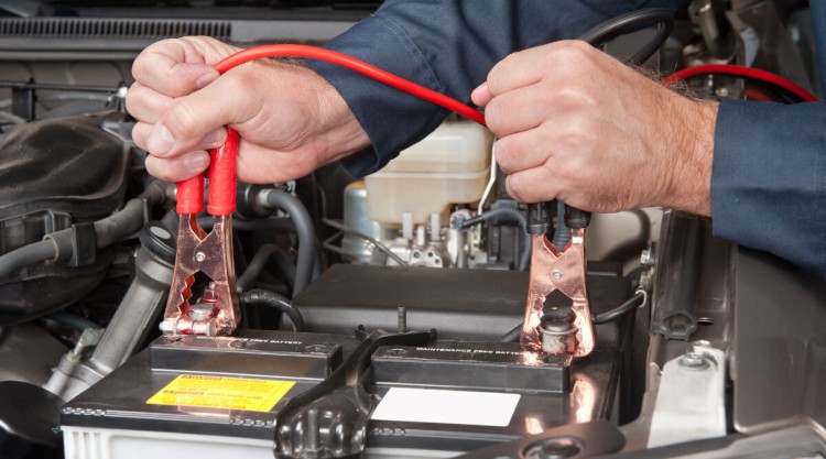 Man plugging cables from a car battery charger onto the battery