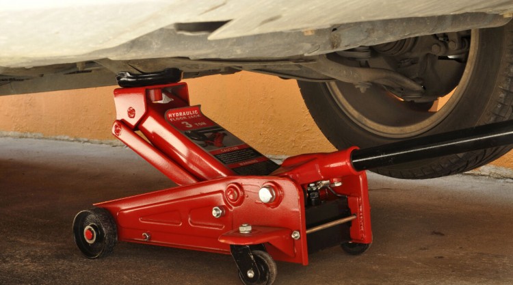 Close up of a red hydraulic floor jack lifting up a car