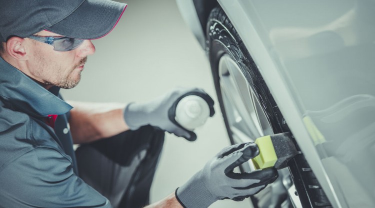 Man in a cap cleaning car tires on a silver car