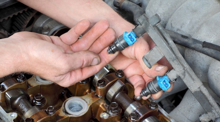 mechanics hand holding fuel injectors above an engine bay