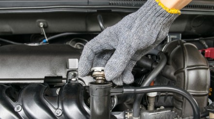 A gloved hand removing the radiator cap in a car engine