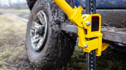 A bright yellow high lift jack being used to raise a 4x4 out of the mud
