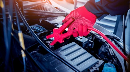 Male gloved hand connecting a jump starter cable to the positive anode of a battery