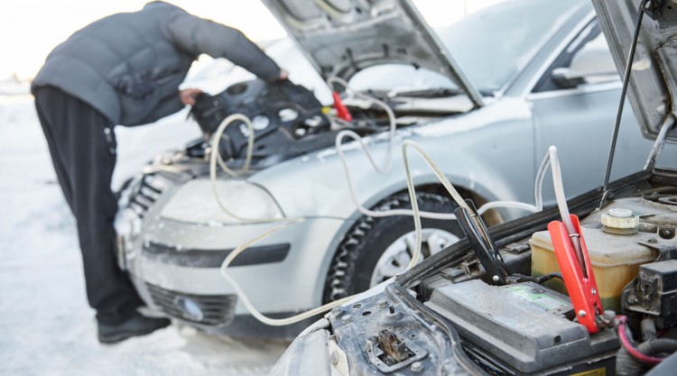 A man starting a car with jumper cables between two vehicles in the snow