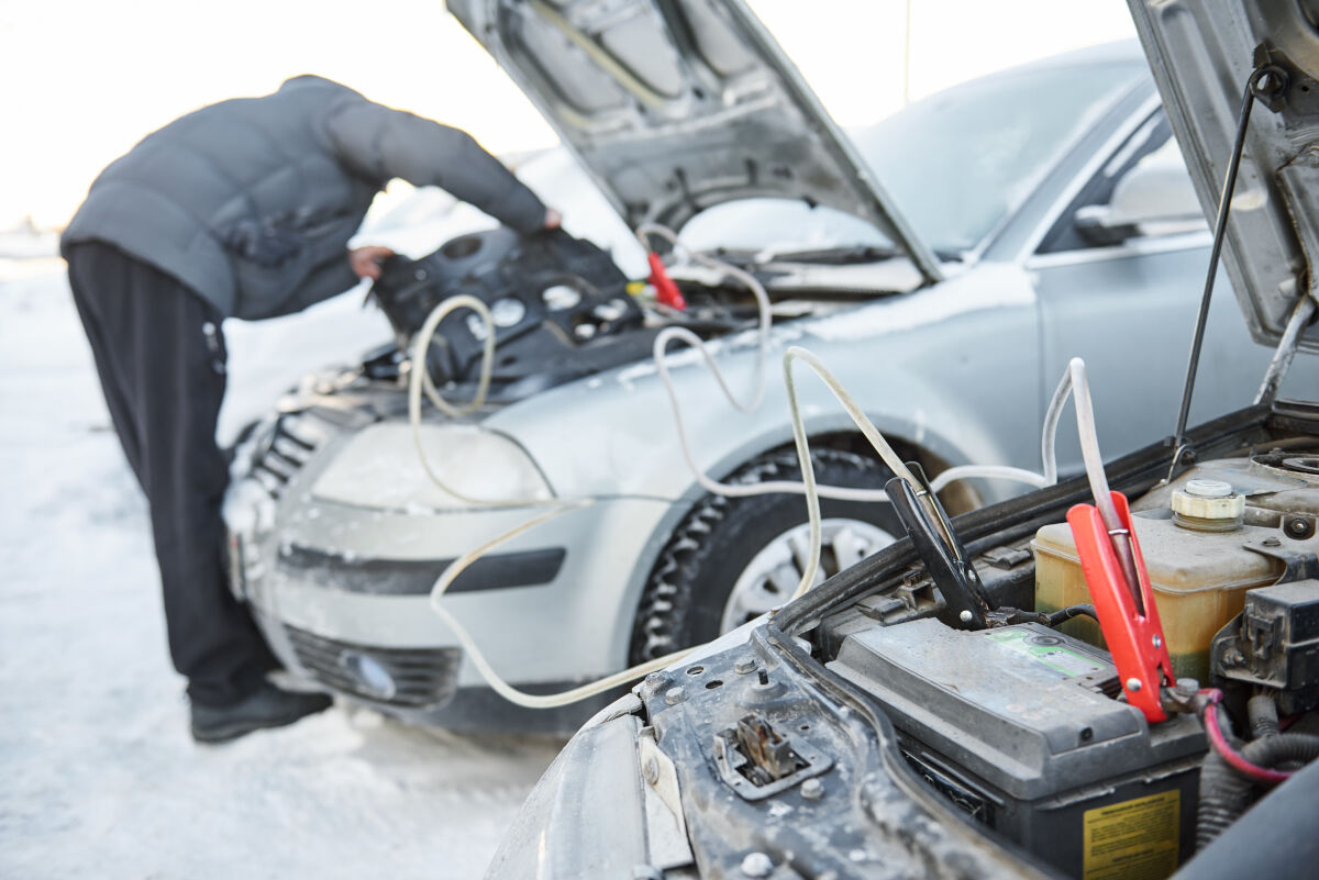 A man starting a car with jumper cables between two vehicles in the snow