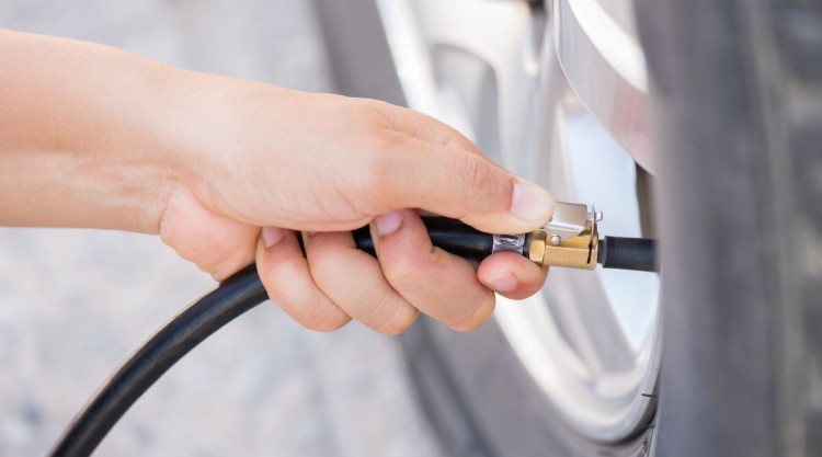 Close up of a hand putting a compressor hose onto the stem of a car tire