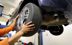 A man removing a tire from a car in the air so he can rotate the tires