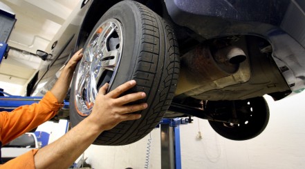A man removing a tire from a car in the air so he can rotate the tires