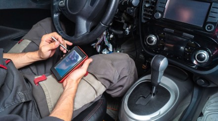 a mechanic reading codes from an OBD2 scan tool while sitting in a car