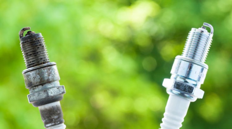 One used and one new spark plug side by side against a green background