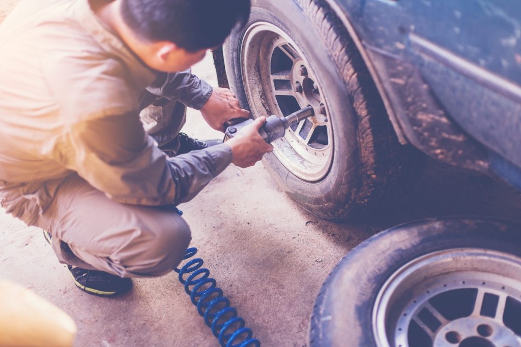 Man using air compressor powered tools to remove a car wheel