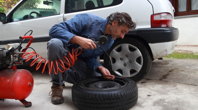 Man working with air compressor from home garage inflating a tyre removed from car