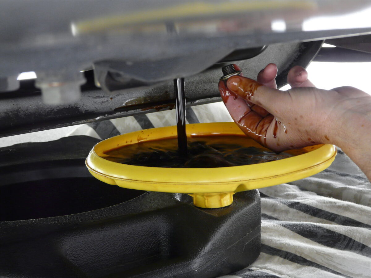 Close up of car being drained of oil, into a yellow funnel.