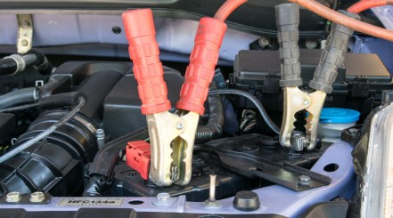 Car battery charger clamps connected to a battery inside a car engine compartment