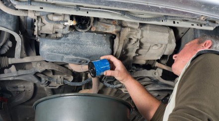 Mechanic under a lifted car removing an oil filter