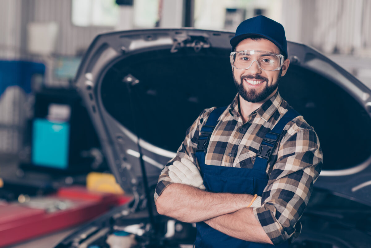 A mechanic wearing gloves adn glasses, with folded arms