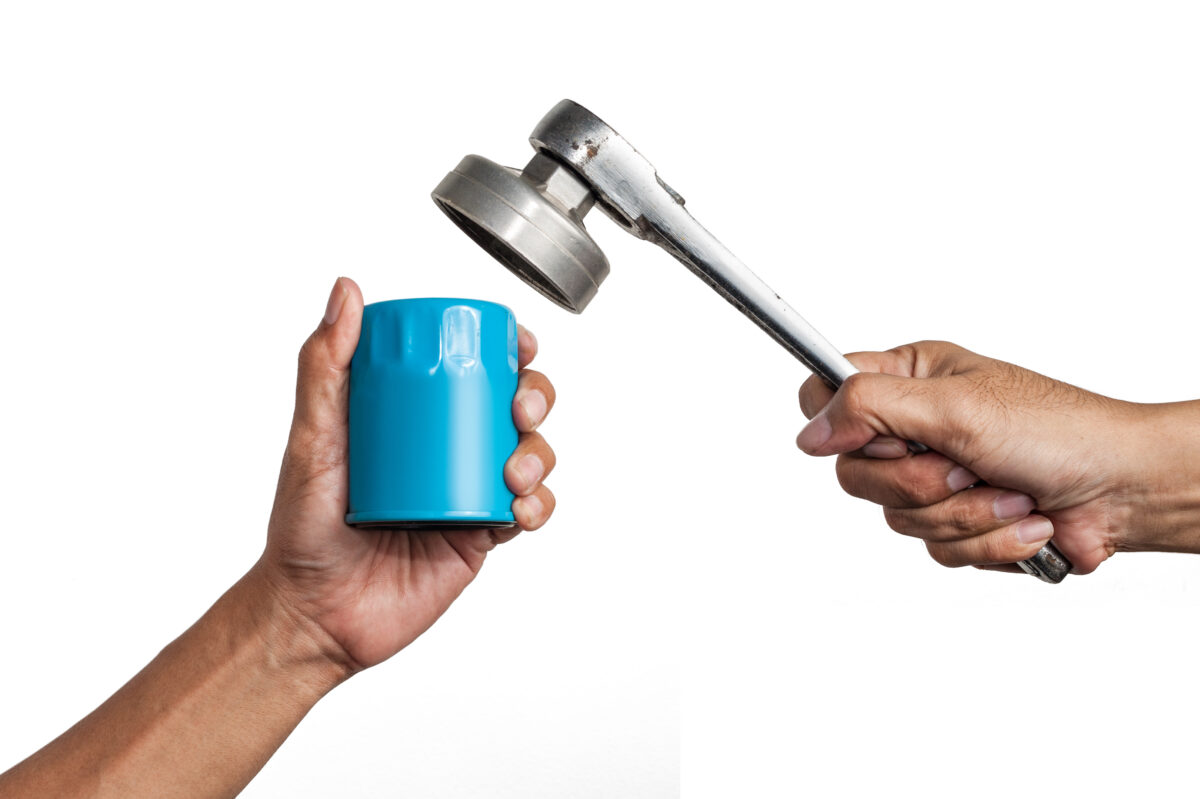 A mechanics hands holding a socket style oil filter wrnech and oil filter, isolated on white