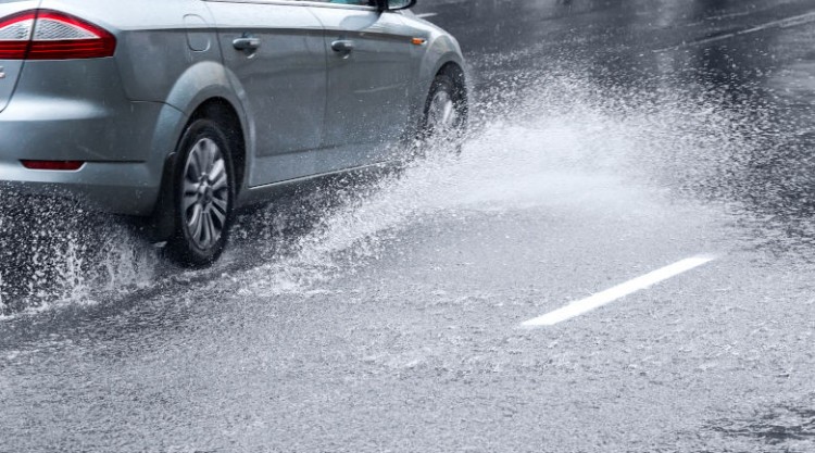 Side view of silver car driving in heavy rain