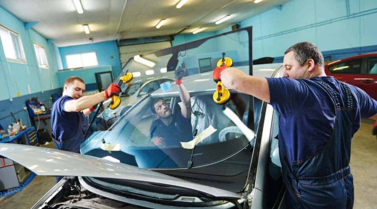 Workers in a garage repair shop replacing a car