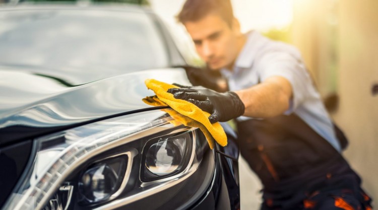 A man holding a microfiber cloth polishing a car after washing it