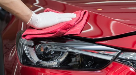 Mans gloved hand applying car paint sealant to the front end of a red car