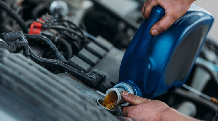 Close up of mans hands puring high mileage oil into an older engine