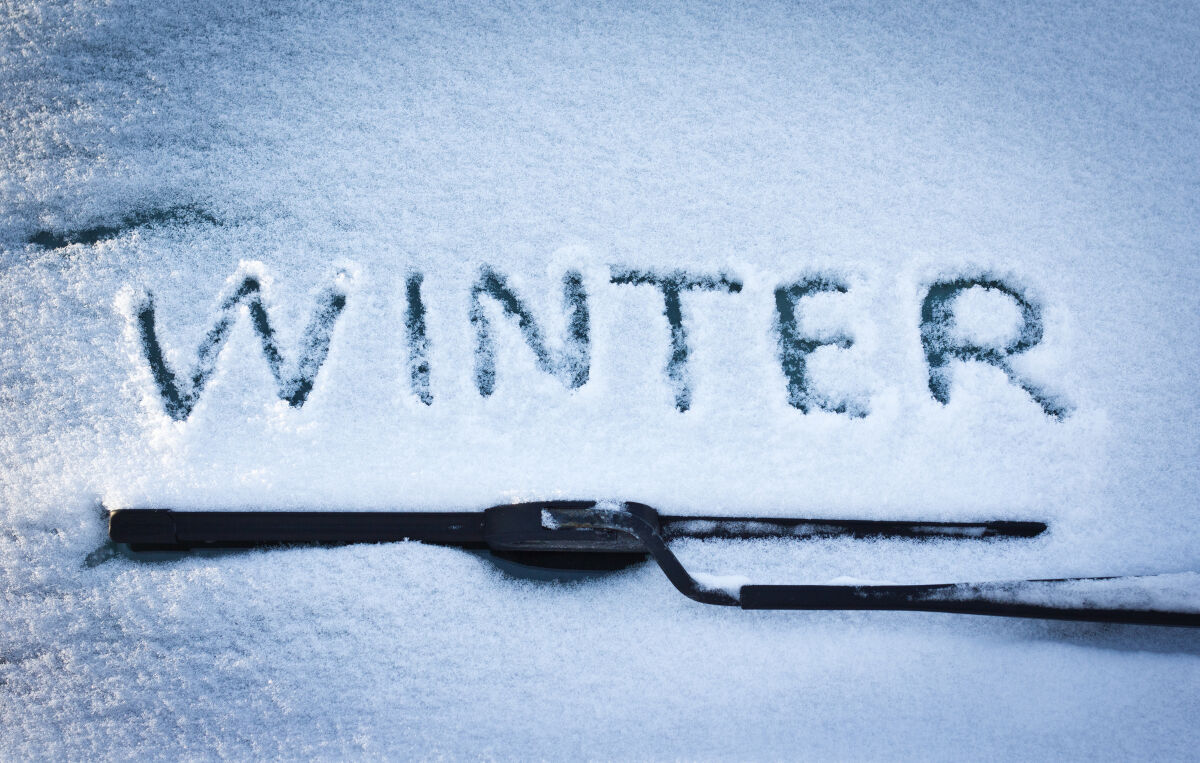 Close up of winter wiper blades, and the word 'winter' written in snow on the windshield