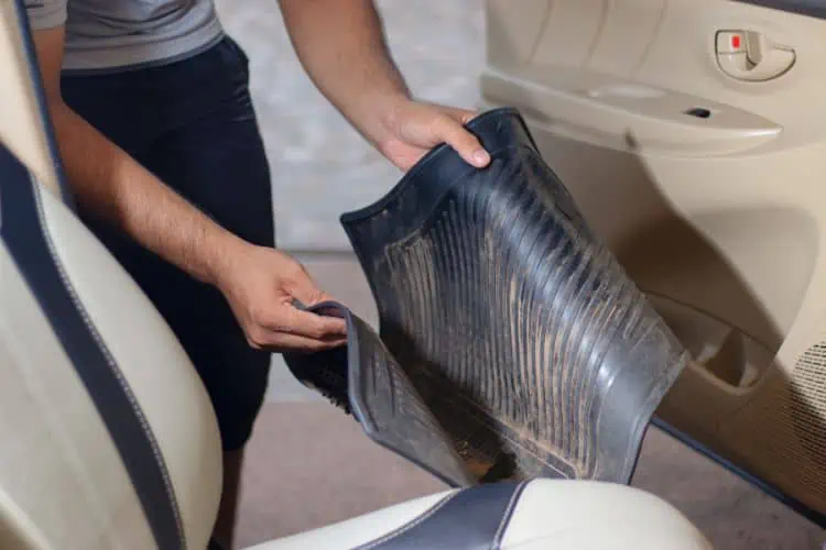 Man removing car floor mat with dirt on it from the car 