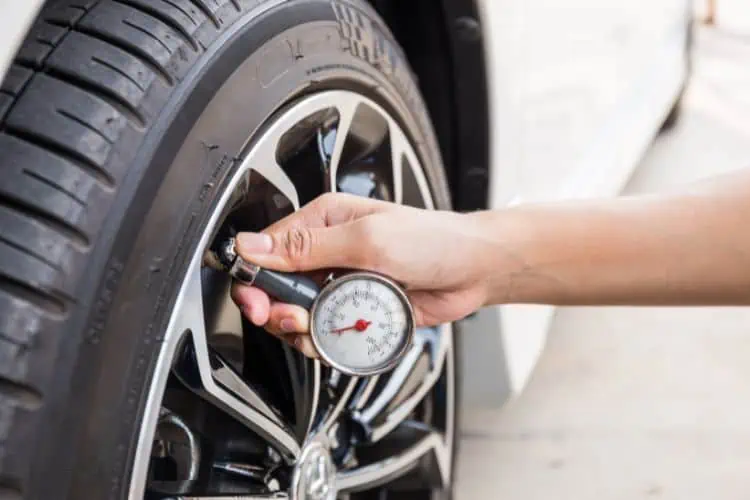Person checking car tire pressure with a pressure gauge