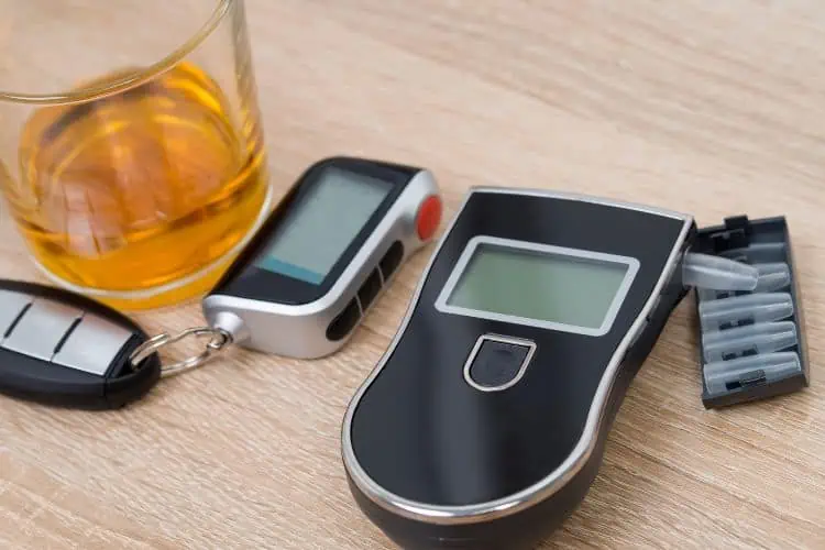 A portable breathalyzer with extra mouthpieces on a table beside car keys and a drink 