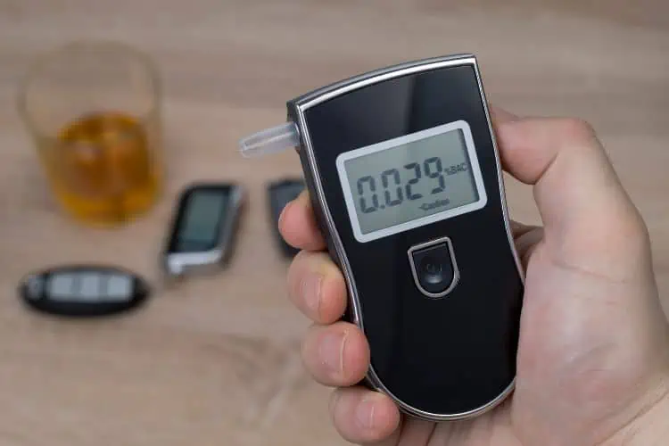 A reading on a portable breathalyzer with car keys and a drink  in the background 