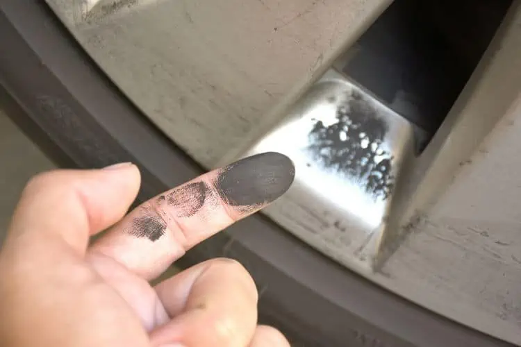 Black brake pad dust on wheel rim and finger 