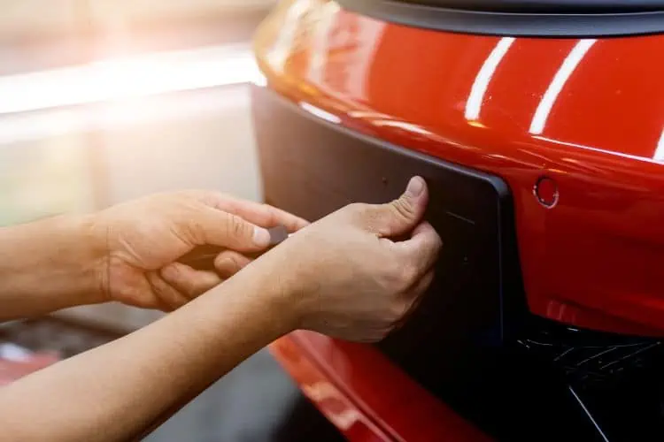 Man fitting black matt license plate from onto red car