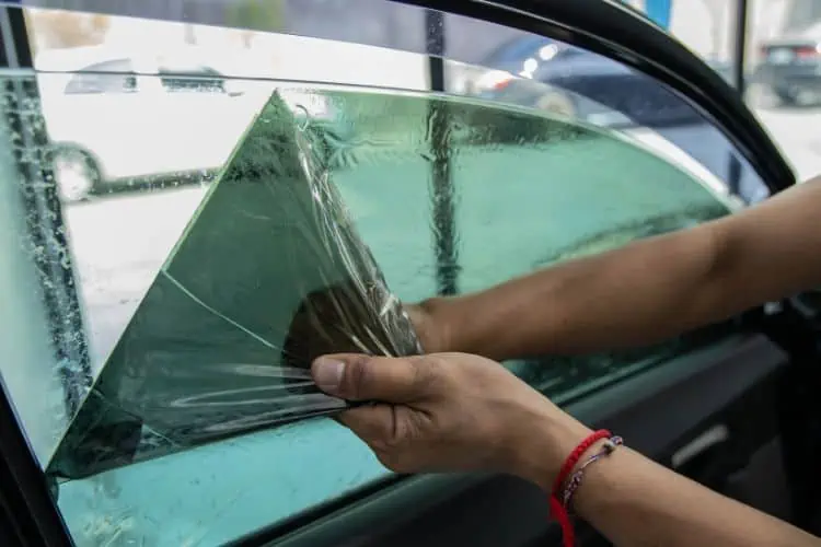 Man pulling tint off car window leaving adhesive marks on car window