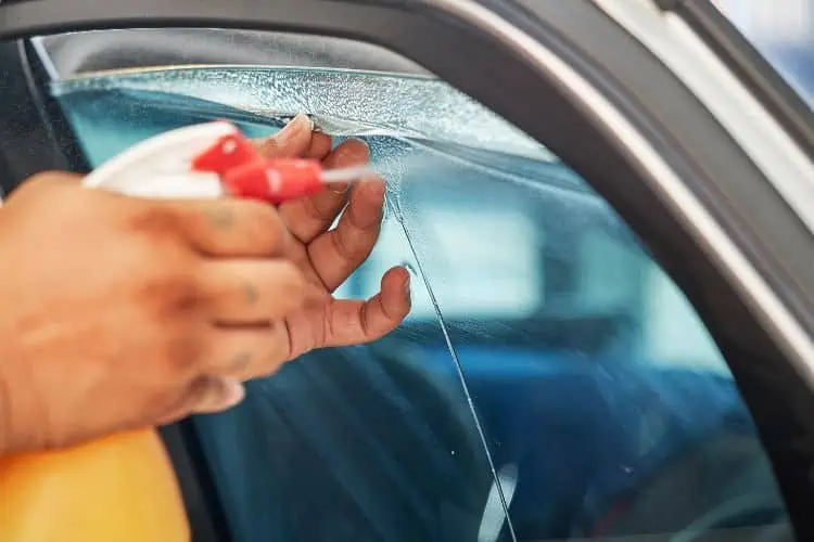 Man spraying ammonia onto car window as he peels tint off