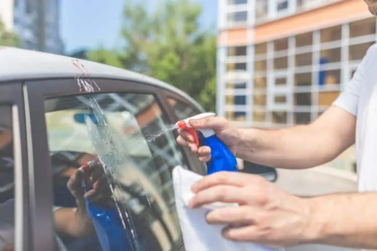 Man spraying detailer onto bird poop stained car window 